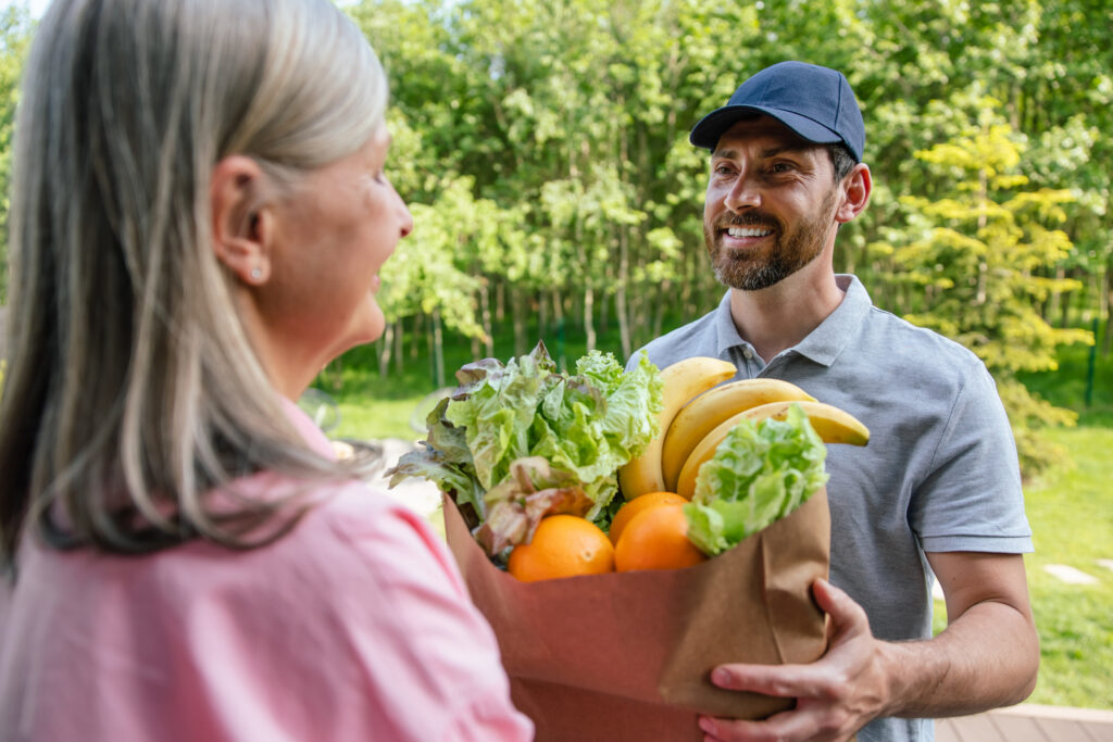 A man holding a paper bag filled with fresh fruit and vegetables.