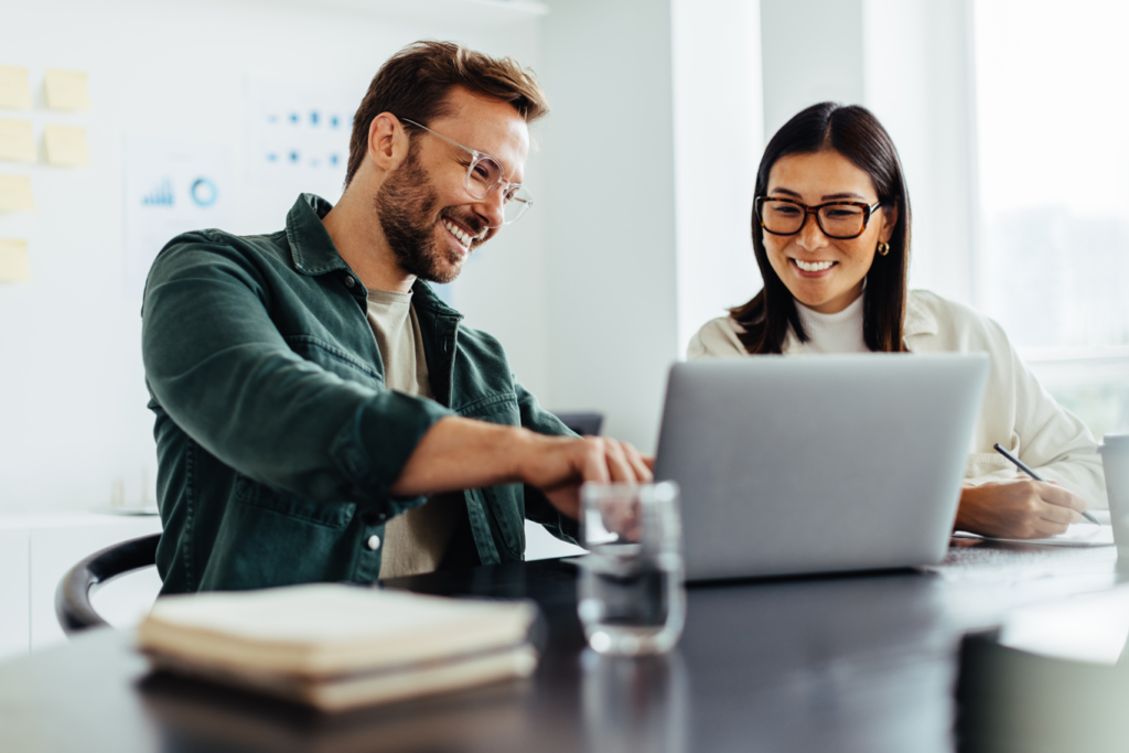 Man and woman wearing glasses discussing debt while looking at laptop in modern office