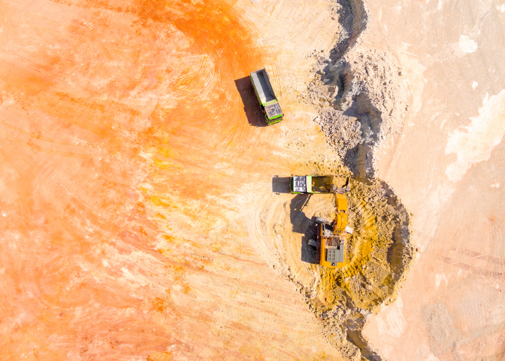 Aerial view of a truck driving on a dirt road through a rural mining landscape.