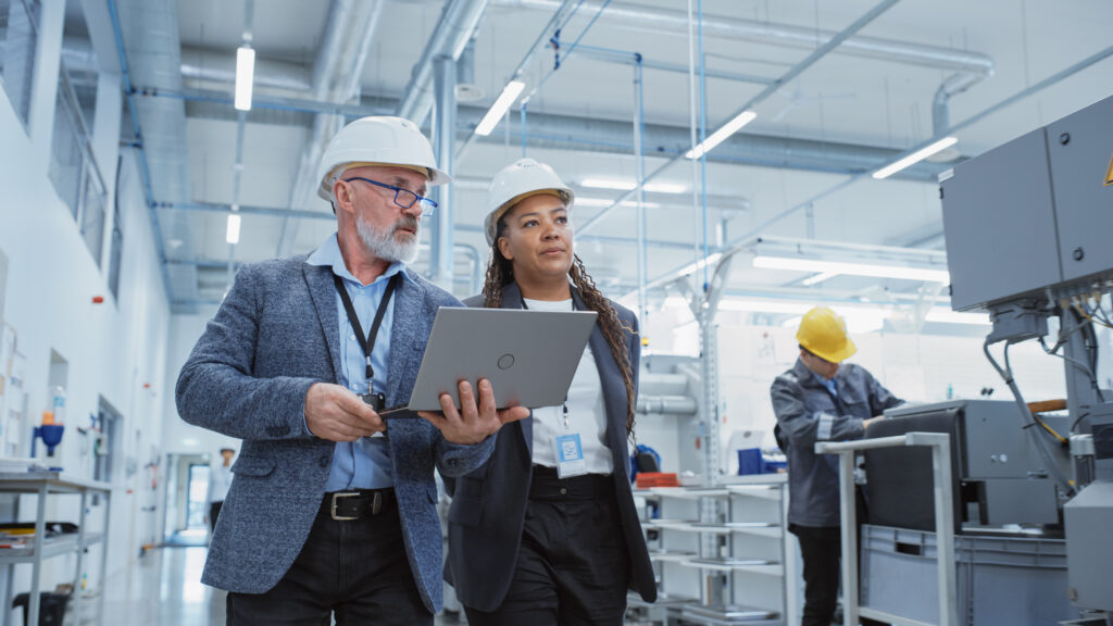 Two workers in hard hats examining digital plans on a tablet at a manufacturing site.