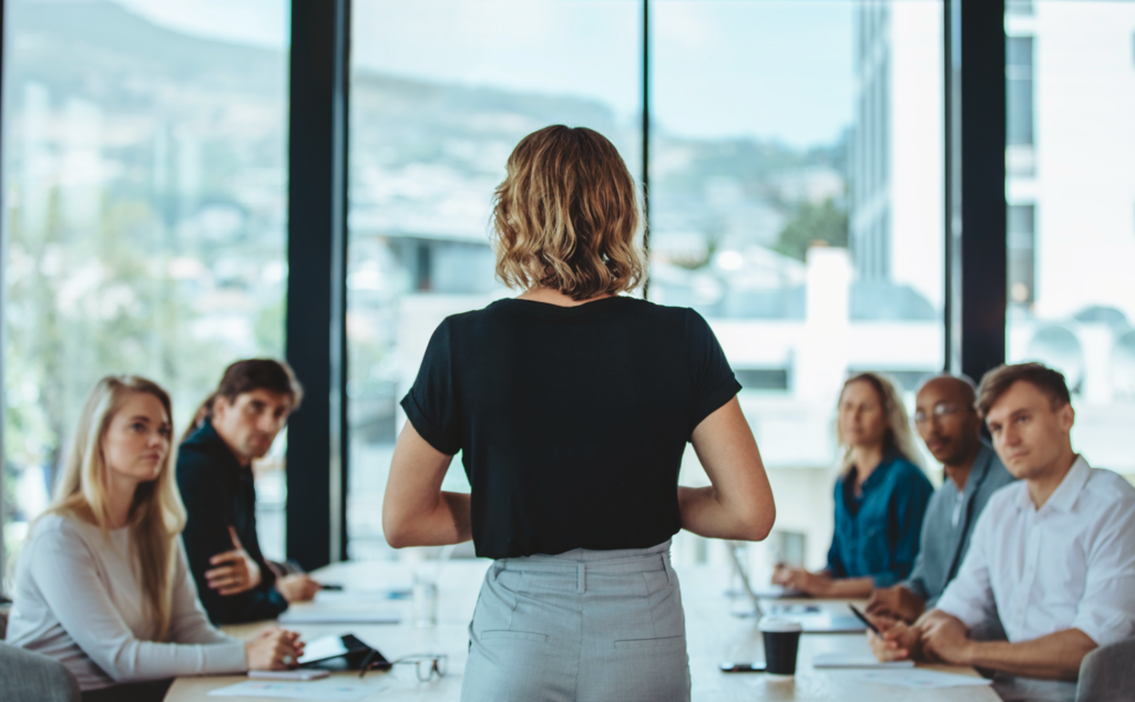 Female standing out front and leading group staff meeting in board room of modern office