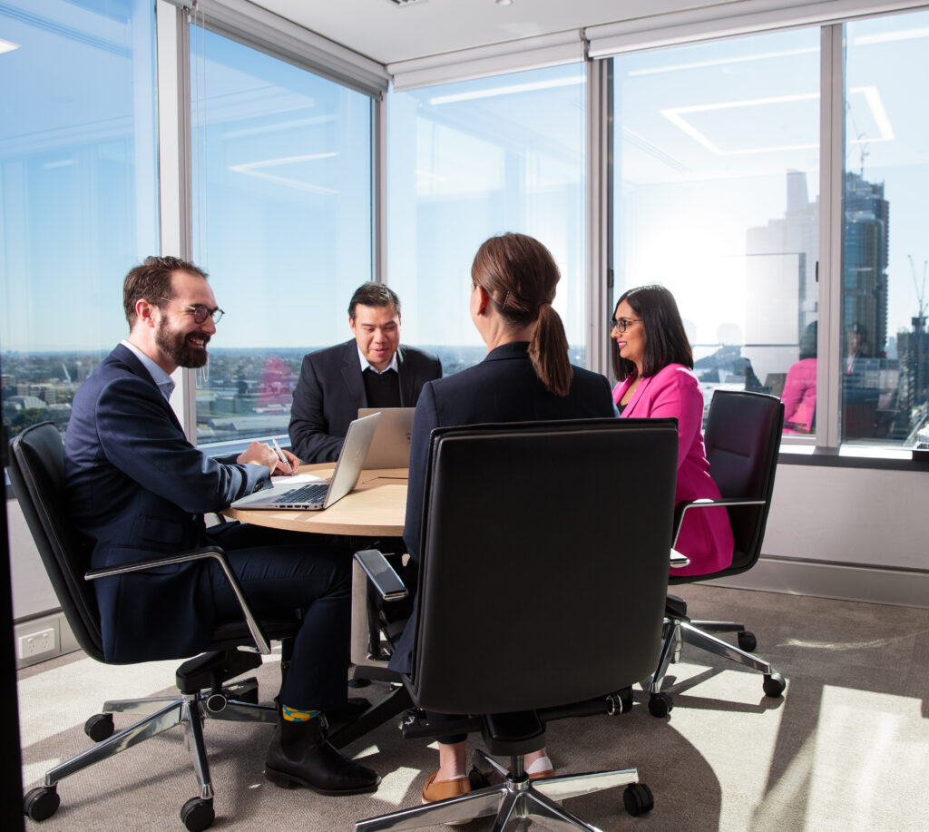 four people in meeting room at round table working and smiling